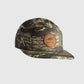 A camouflage 5-panel cap with a brown circular patch on the front featuring a LOC Heron logo, shown against a light brown background.