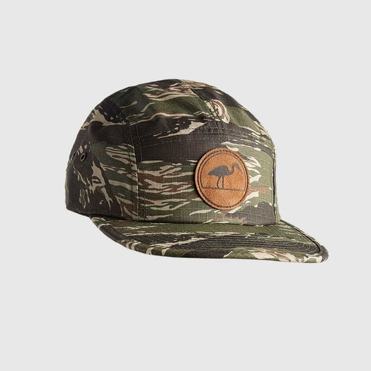 A camouflage 5-panel cap with a brown circular patch on the front featuring a LOC Heron logo, shown against a light brown background.